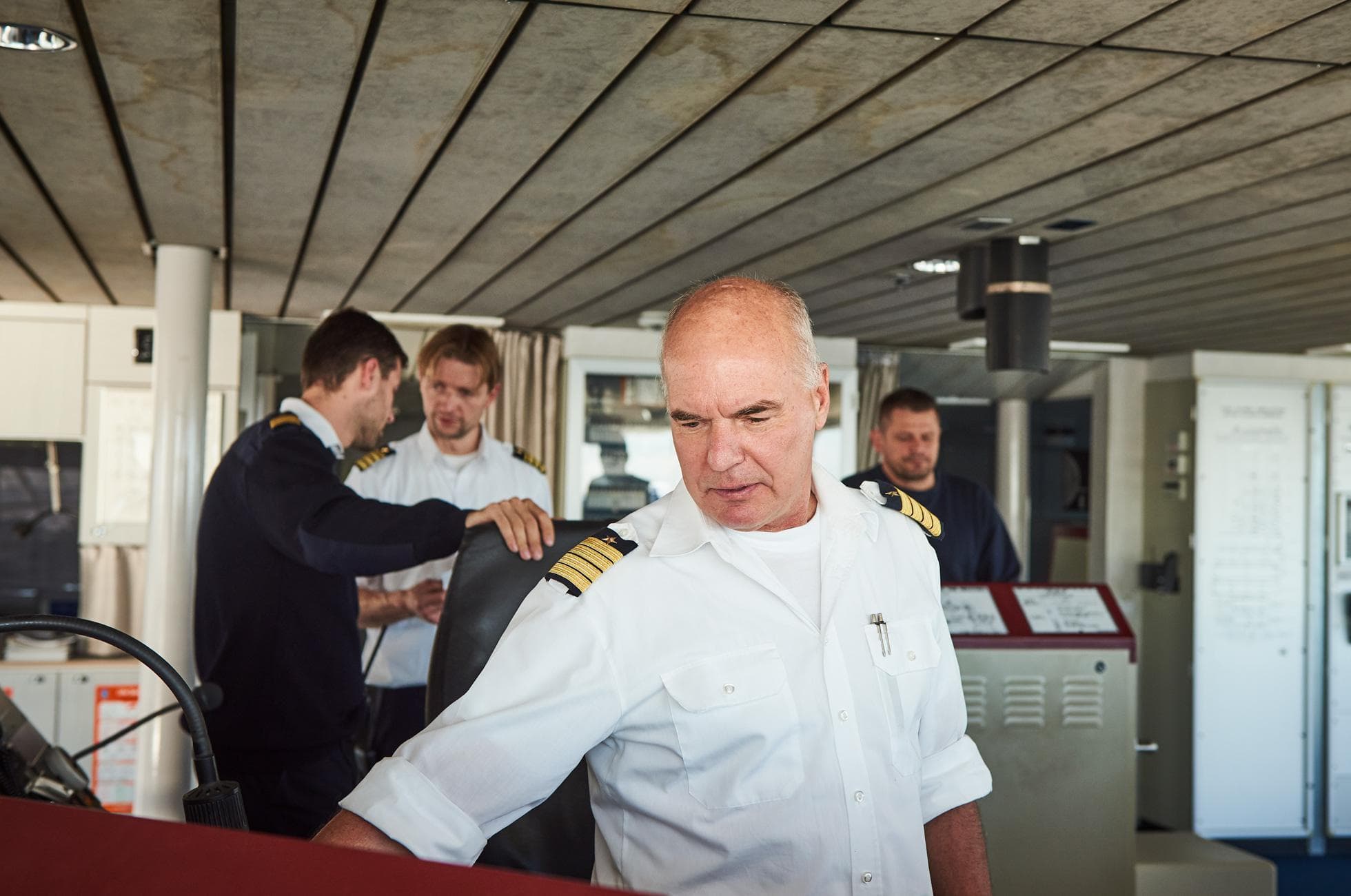 Photograph of ship's bridge with captain in foreground and crew in the background